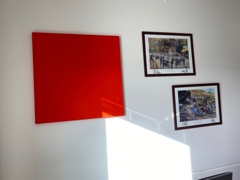 Panneau acoustique carré rouge à côté de tirages encadrés au mur