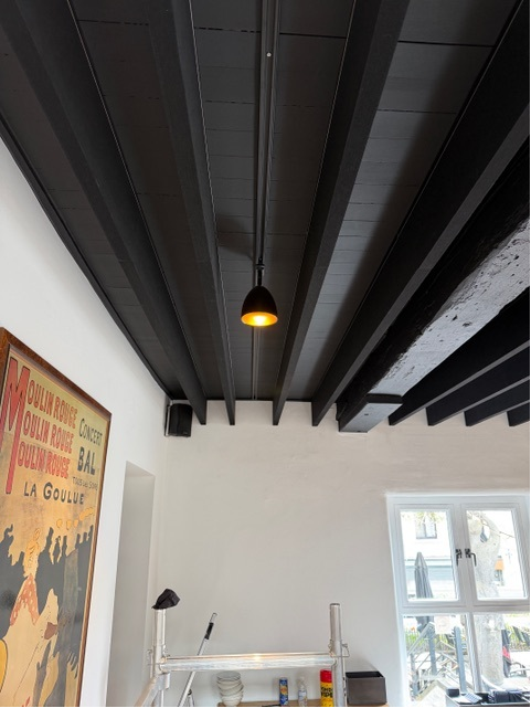 Plafond à poutres peintes en noir avec absorption acoustique entre les poutres dans un bistrot