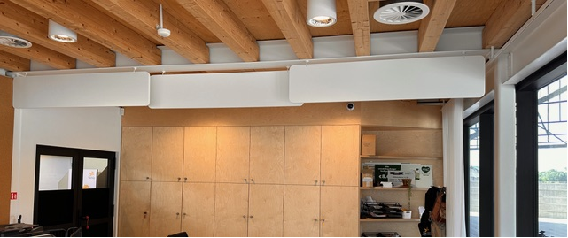 Baffles acoustiques blancs au-dessus d'une zone cuisine avec armoires en bois et plafond à poutres