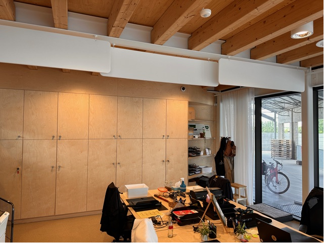 Baffles acoustiques blancs dans un espace de travail avec plafond en bois et grande baie vitrée