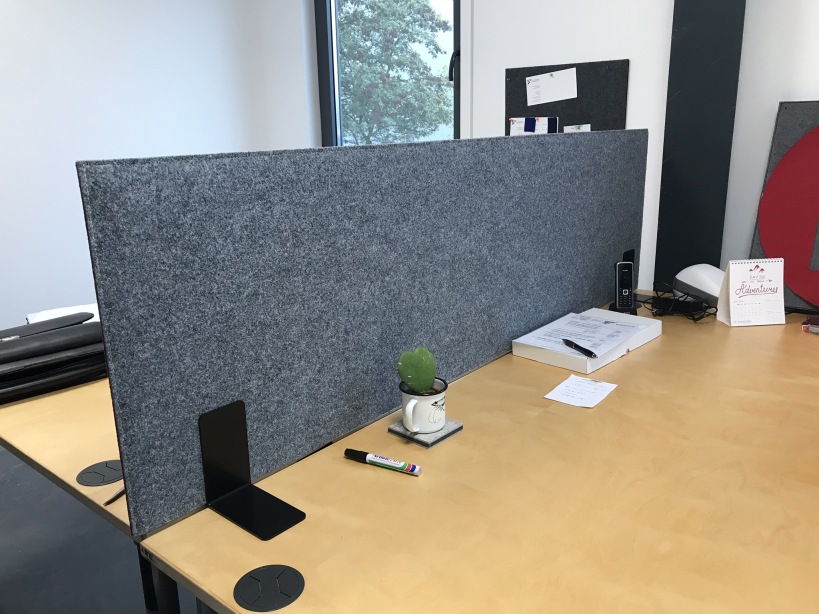 Écran de bureau acoustique en feutre gris sur plan de travail partagé près de la fenêtre