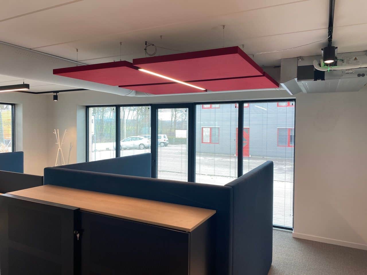 Îlot de plafond acoustique rouge avec éclairage intégré au-dessus d'une zone lounge
