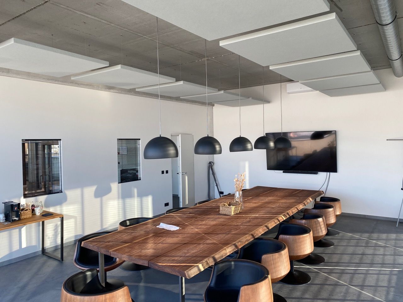 Îlots de plafond acoustiques blancs au-dessus d'une table de réunion en bois avec plafond béton