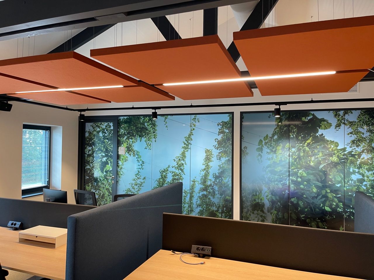 Îlots acoustiques orange au-dessus d'un poste de travail avec mur photo vert