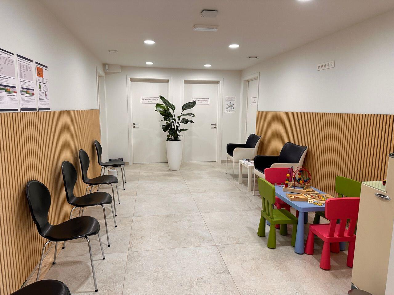 Salle d'attente avec mur en lattes de bois et coin enfants dans un cabinet de groupe
