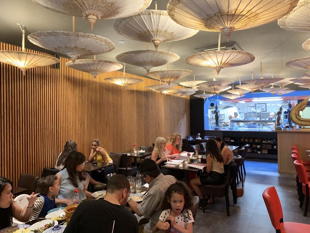 Zelfde restaurantzaal na akoestische ingreep met houten lattenwand en decoratieve parasol-elementen aan het plafond