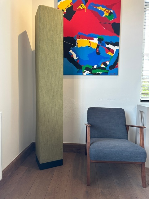 Totem acoustique vert à côté d'une chaise design et d'une toile colorée